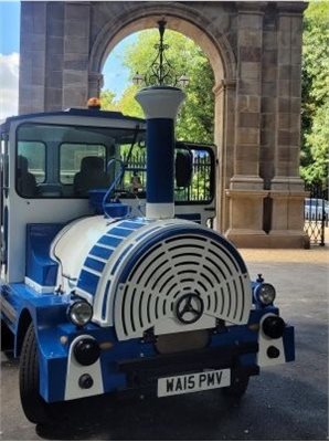 Blue and white land train in front of a large stone archway