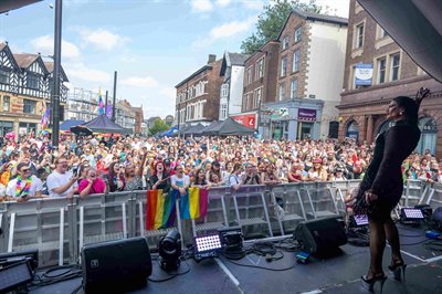 Musician on a stage in front of a large crowd with rainbow flags