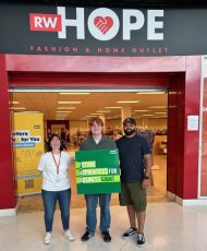 Three people stood under a shop sign saying Rebuild with Hope